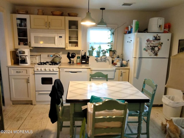 kitchen with white cabinetry, sink, light wood-type flooring, hanging light fixtures, and white appliances