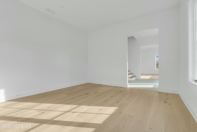 unfurnished room featuring light wood finished floors, visible vents, stairs, and baseboards