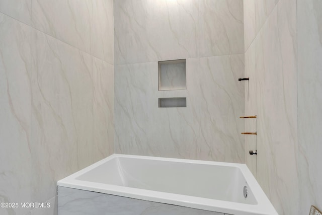 full bath featuring tile walls and a combined bath / shower with marble appearance