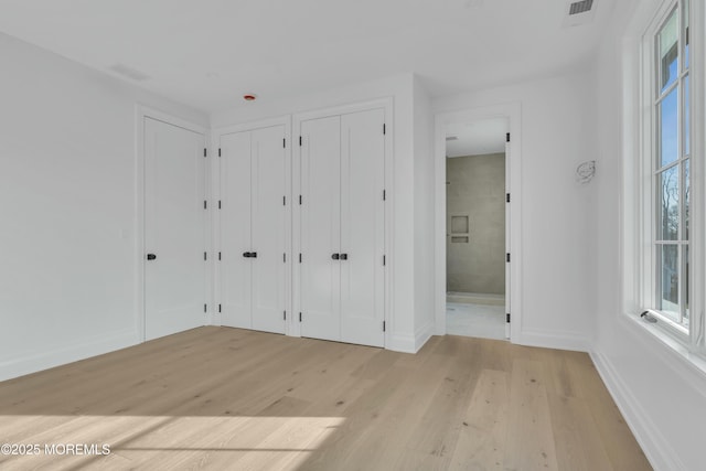 unfurnished bedroom with visible vents, multiple closets, connected bathroom, light wood finished floors, and baseboards