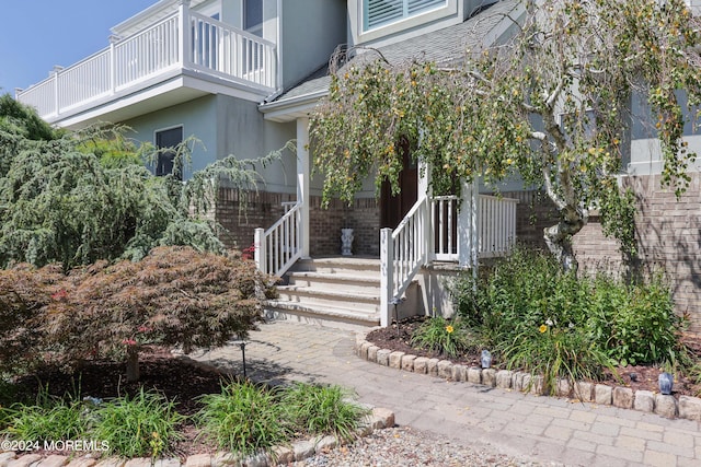 property entrance featuring brick siding, a shingled roof, a balcony, and stucco siding