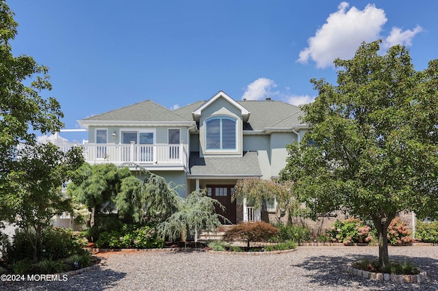 view of front facade featuring a shingled roof, a balcony, and stucco siding