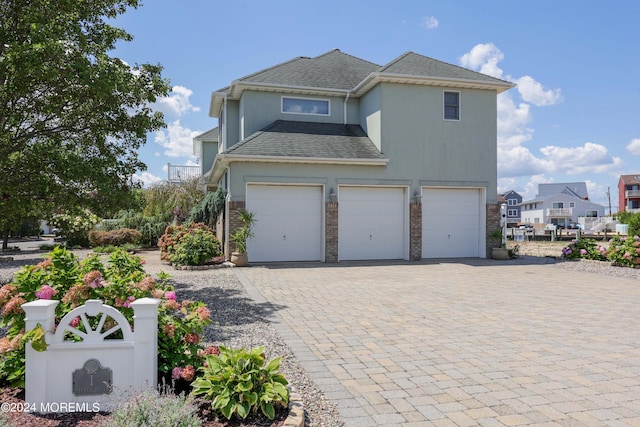 view of front of home with an attached garage, a shingled roof, brick siding, fence, and decorative driveway