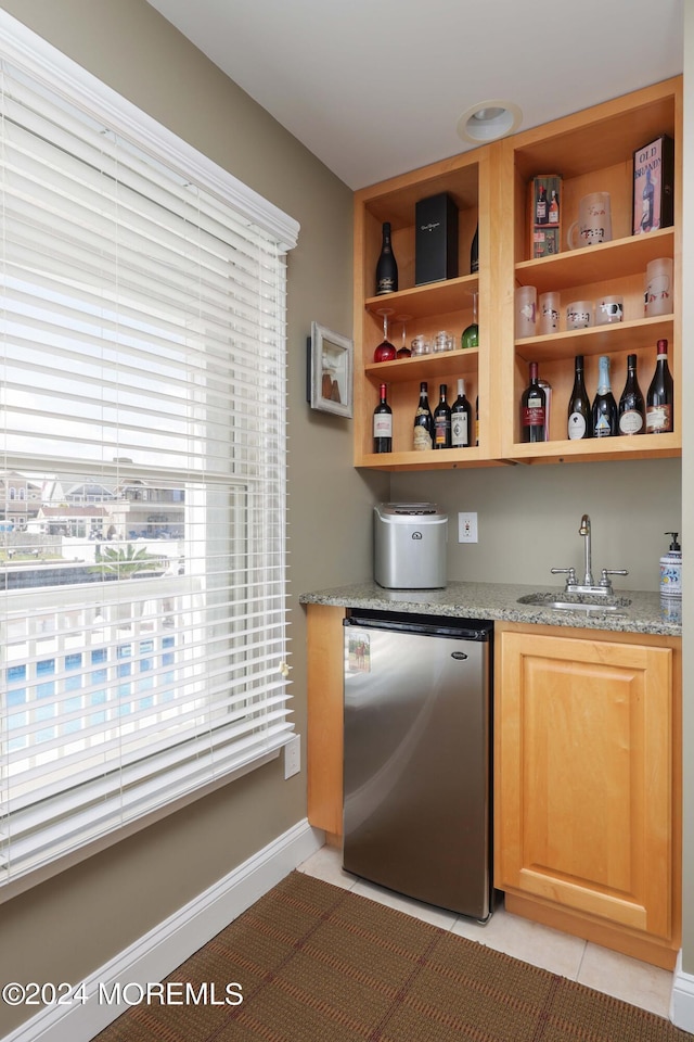 bar featuring light tile patterned floors, baseboards, dishwashing machine, wet bar, and a sink