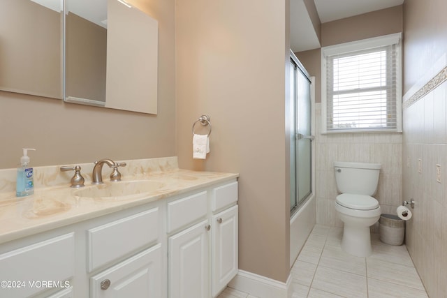 full bathroom featuring tile patterned flooring, toilet, shower / bath combination with glass door, vanity, and tile walls