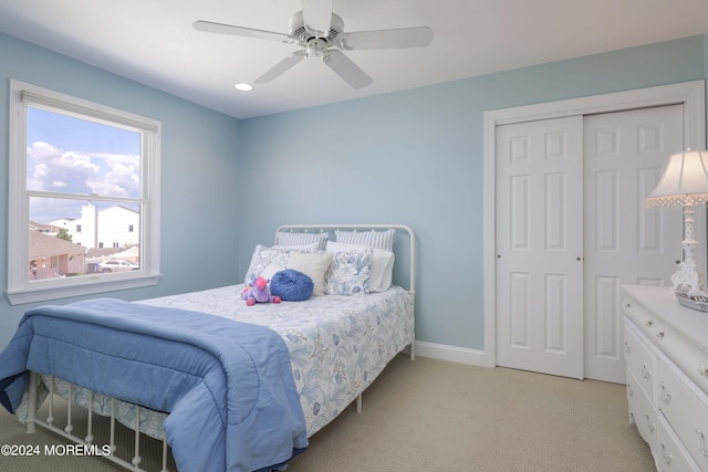 bedroom with a closet, light colored carpet, ceiling fan, and baseboards