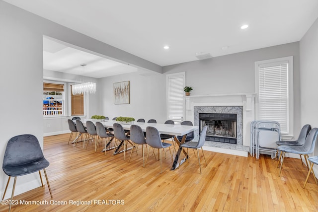 dining space with wood-type flooring, an inviting chandelier, and a high end fireplace