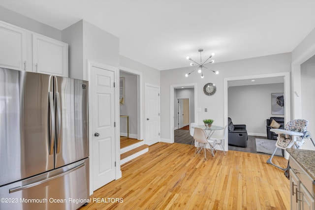 kitchen with stainless steel refrigerator, a notable chandelier, light hardwood / wood-style floors, and white cabinets