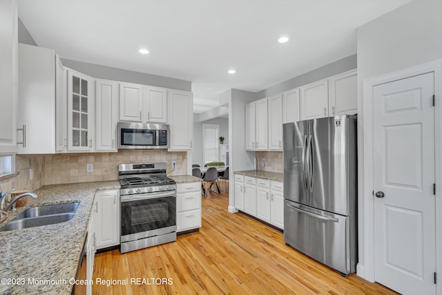 kitchen featuring appliances with stainless steel finishes, white cabinetry, sink, light hardwood / wood-style floors, and light stone countertops