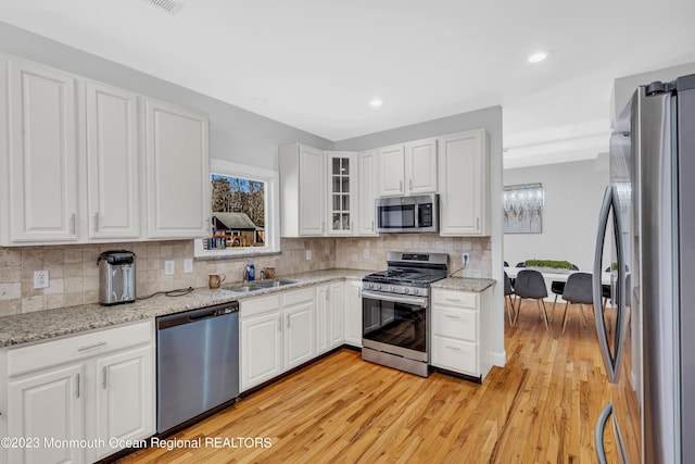 kitchen featuring sink, light stone counters, appliances with stainless steel finishes, decorative backsplash, and white cabinets