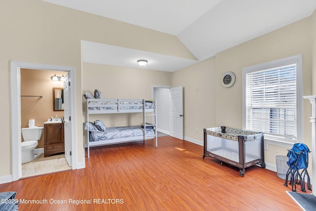 bedroom with lofted ceiling, ensuite bathroom, and wood-type flooring