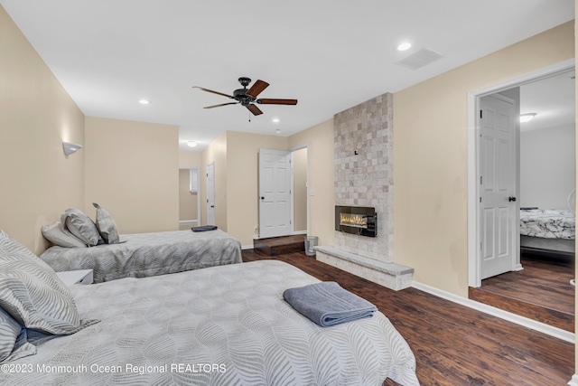 bedroom featuring ceiling fan, dark hardwood / wood-style floors, and a stone fireplace