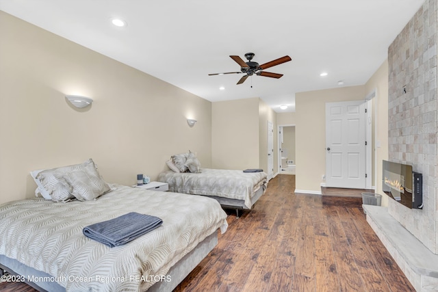 bedroom with ceiling fan, dark wood-type flooring, and a fireplace