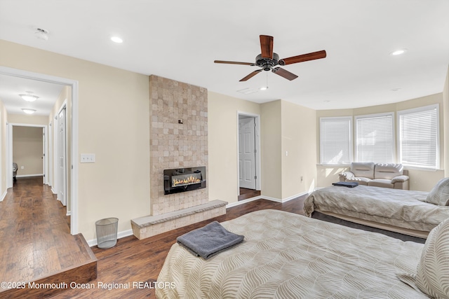 bedroom with a tiled fireplace, dark wood-type flooring, and ceiling fan