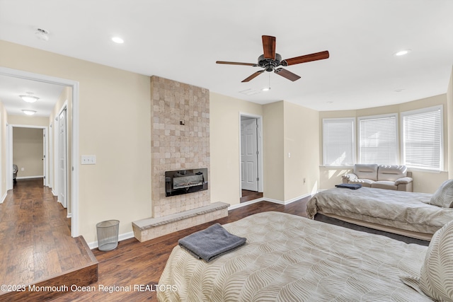 bedroom with ceiling fan, a large fireplace, and dark hardwood / wood-style floors