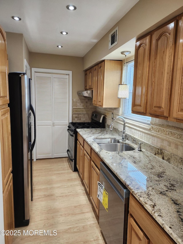 kitchen with sink, light wood-type flooring, stainless steel appliances, and light stone countertops