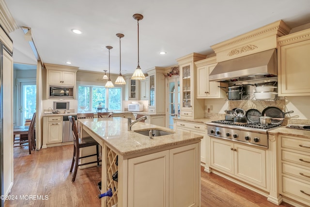 kitchen with hanging light fixtures, glass insert cabinets, appliances with stainless steel finishes, a kitchen island with sink, and a sink