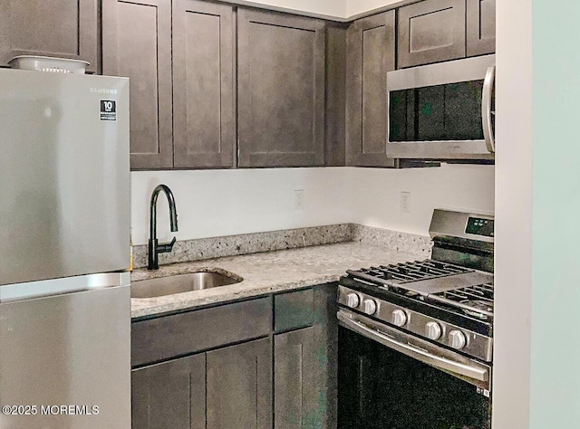 kitchen with appliances with stainless steel finishes, light stone counters, and sink