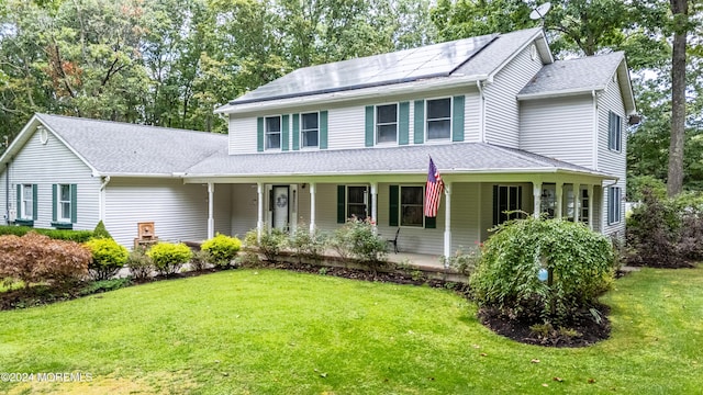 view of front facade featuring covered porch, solar panels, a shingled roof, and a front yard