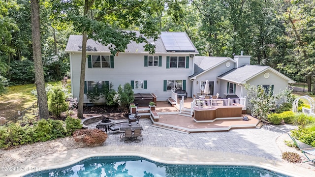 rear view of property with a hot tub, a fire pit, solar panels, a deck, and a patio area