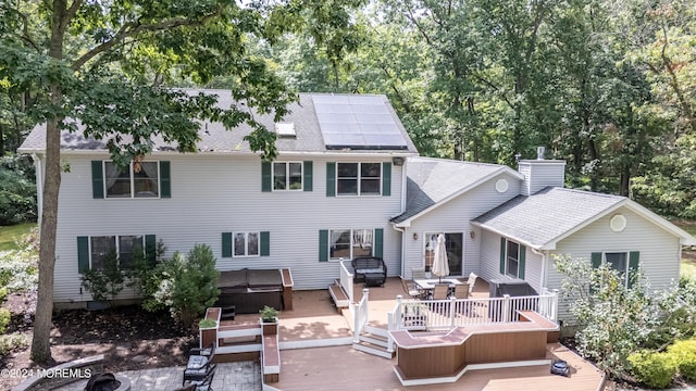 back of house with roof with shingles, a hot tub, outdoor dining space, roof mounted solar panels, and a wooden deck