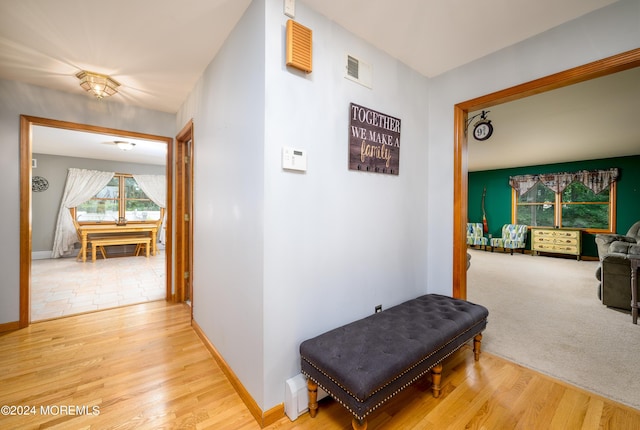 hallway featuring light wood-style floors, baseboards, visible vents, and light colored carpet