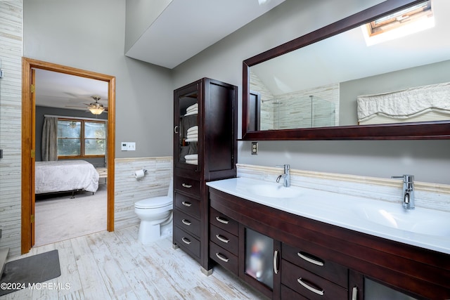 ensuite bathroom with connected bathroom, toilet, a wainscoted wall, a sink, and double vanity