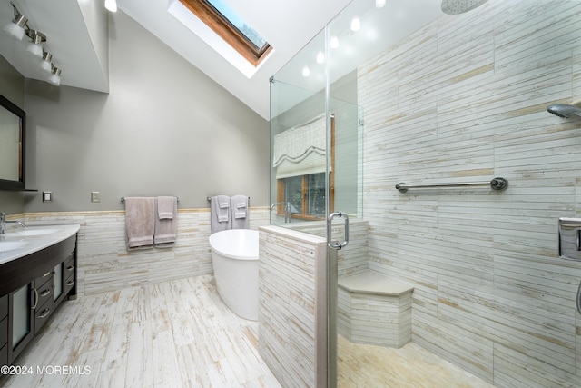 full bath featuring a wainscoted wall, tile walls, a freestanding bath, lofted ceiling with skylight, and a stall shower