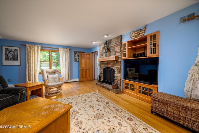 living room featuring a stone fireplace, wood finished floors, and visible vents