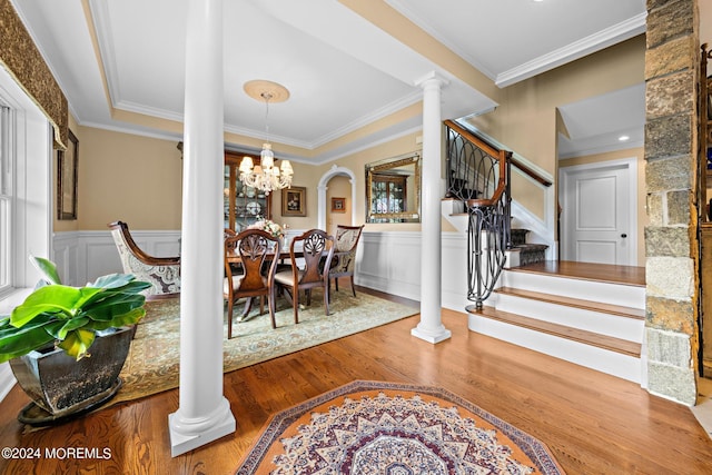 dining space with ornamental molding, an inviting chandelier, decorative columns, and wood-type flooring