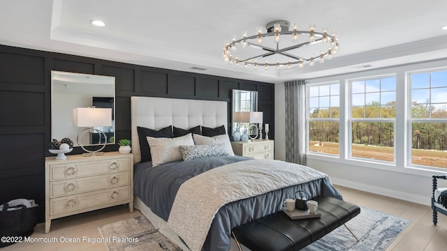 bedroom featuring a notable chandelier, a tray ceiling, and light wood-type flooring