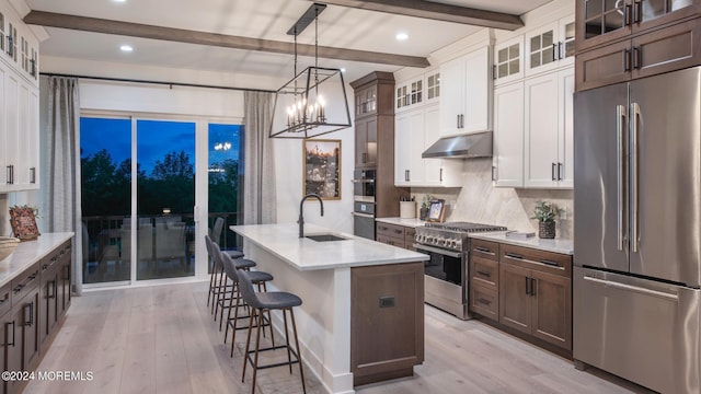 kitchen featuring high end appliances, beam ceiling, white cabinets, and sink