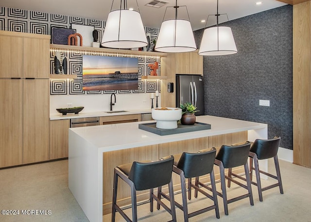 kitchen with a breakfast bar, sink, a kitchen island, stainless steel fridge, and pendant lighting