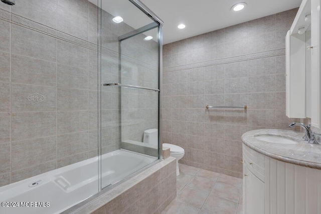 bathroom with vanity, toilet, tile patterned floors, tiled shower / bath, and tile walls