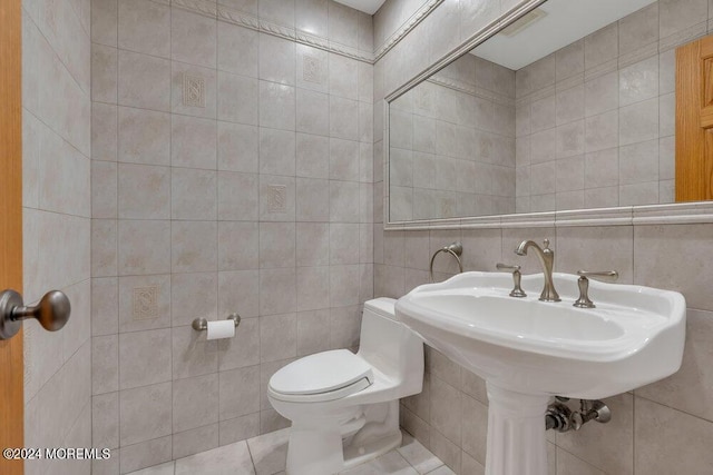 half bath with tile patterned flooring, toilet, and tile walls