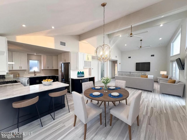 dining area with high vaulted ceiling, light hardwood / wood-style flooring, ceiling fan with notable chandelier, and a healthy amount of sunlight