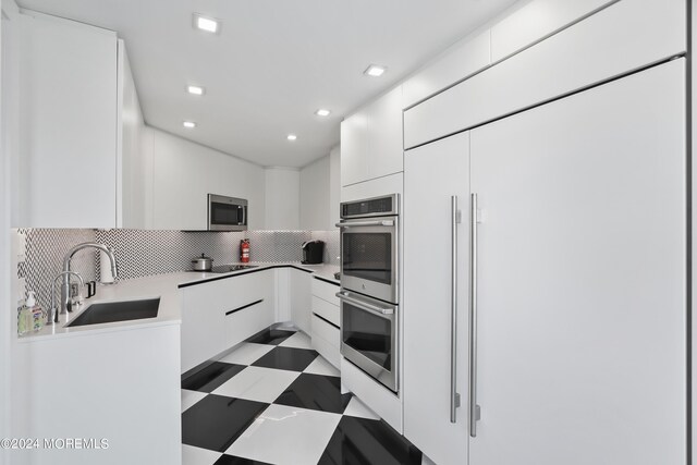 kitchen featuring backsplash, sink, light tile patterned floors, stainless steel appliances, and white cabinets