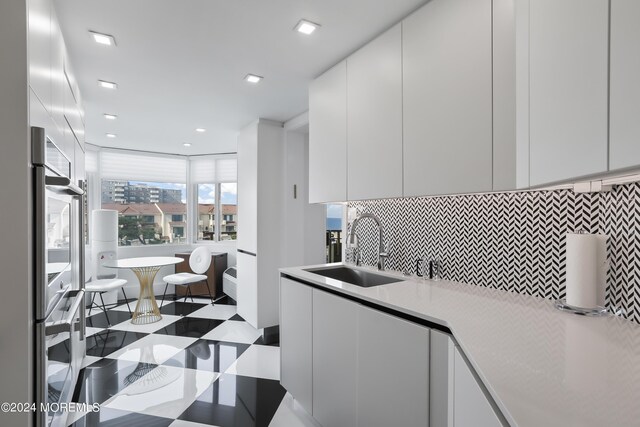 kitchen featuring white cabinetry, multiple ovens, tasteful backsplash, sink, and tile patterned floors