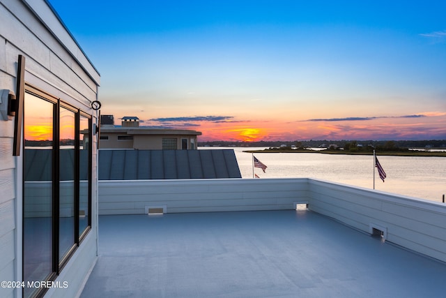 patio terrace at dusk featuring a balcony and a water view