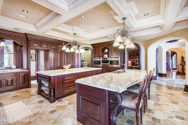 kitchen with a kitchen island with sink, stainless steel oven, light tile patterned floors, and coffered ceiling