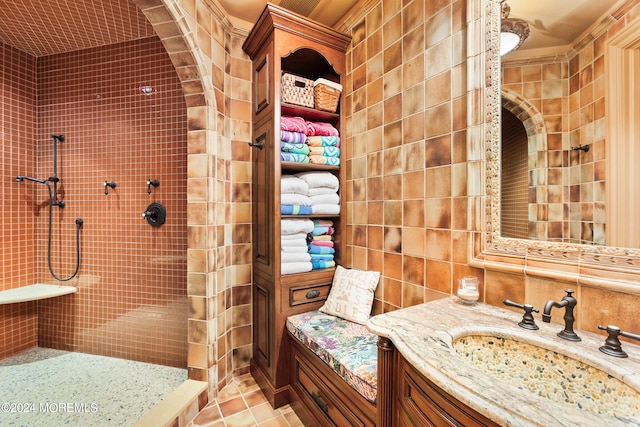 bathroom with tiled shower, tile patterned flooring, vanity, and tile walls