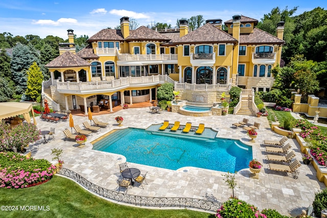 rear view of house with a patio area, a balcony, and a pool with hot tub