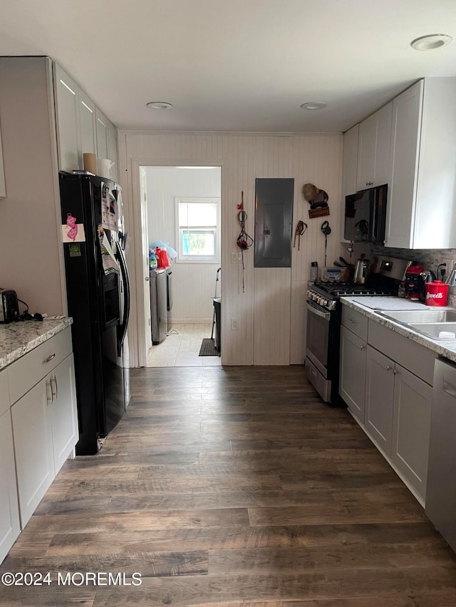 kitchen with washing machine and dryer, black appliances, hardwood / wood-style floors, and light stone countertops