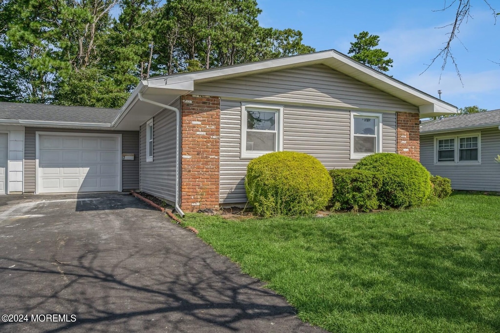 view of side of property featuring driveway, brick siding, a lawn, and an attached garage