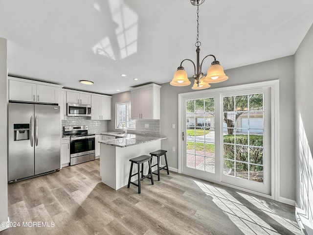 kitchen featuring appliances with stainless steel finishes, light hardwood / wood-style flooring, decorative backsplash, pendant lighting, and white cabinets