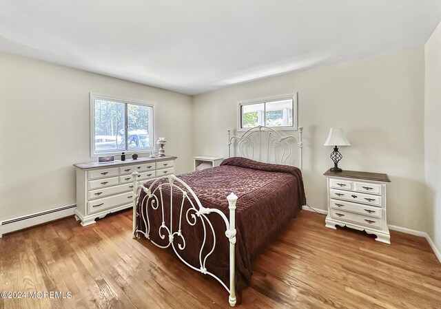 bedroom featuring light hardwood / wood-style flooring, baseboard heating, and multiple windows