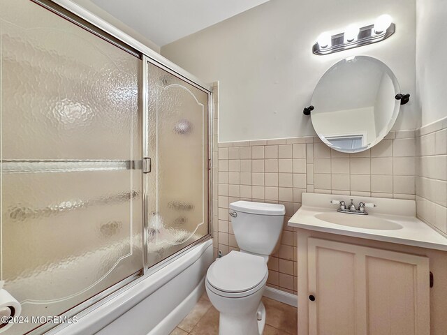 full bathroom with toilet, tile patterned floors, tile walls, bath / shower combo with glass door, and vanity