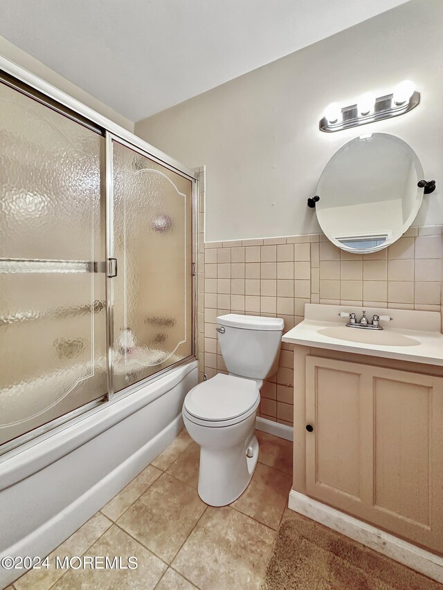 full bathroom featuring toilet, tile patterned floors, shower / bath combination with glass door, tile walls, and vanity