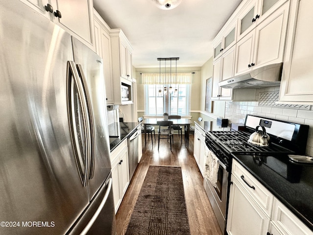 kitchen featuring dark countertops, glass insert cabinets, appliances with stainless steel finishes, decorative light fixtures, and under cabinet range hood