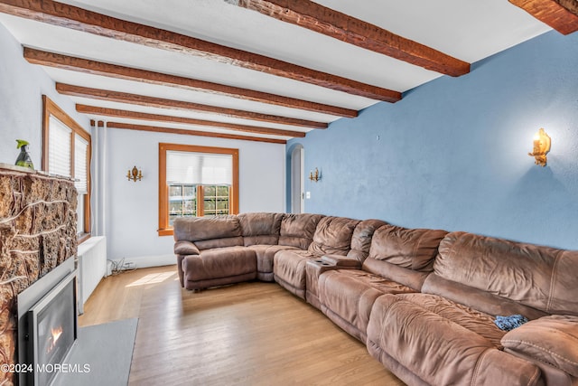 living room featuring light wood-type flooring, beamed ceiling, and a stone fireplace